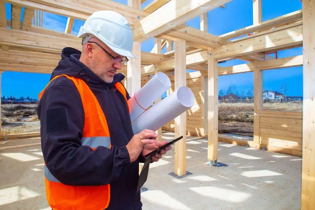 Construction worker with plans at a wooden house frame site.